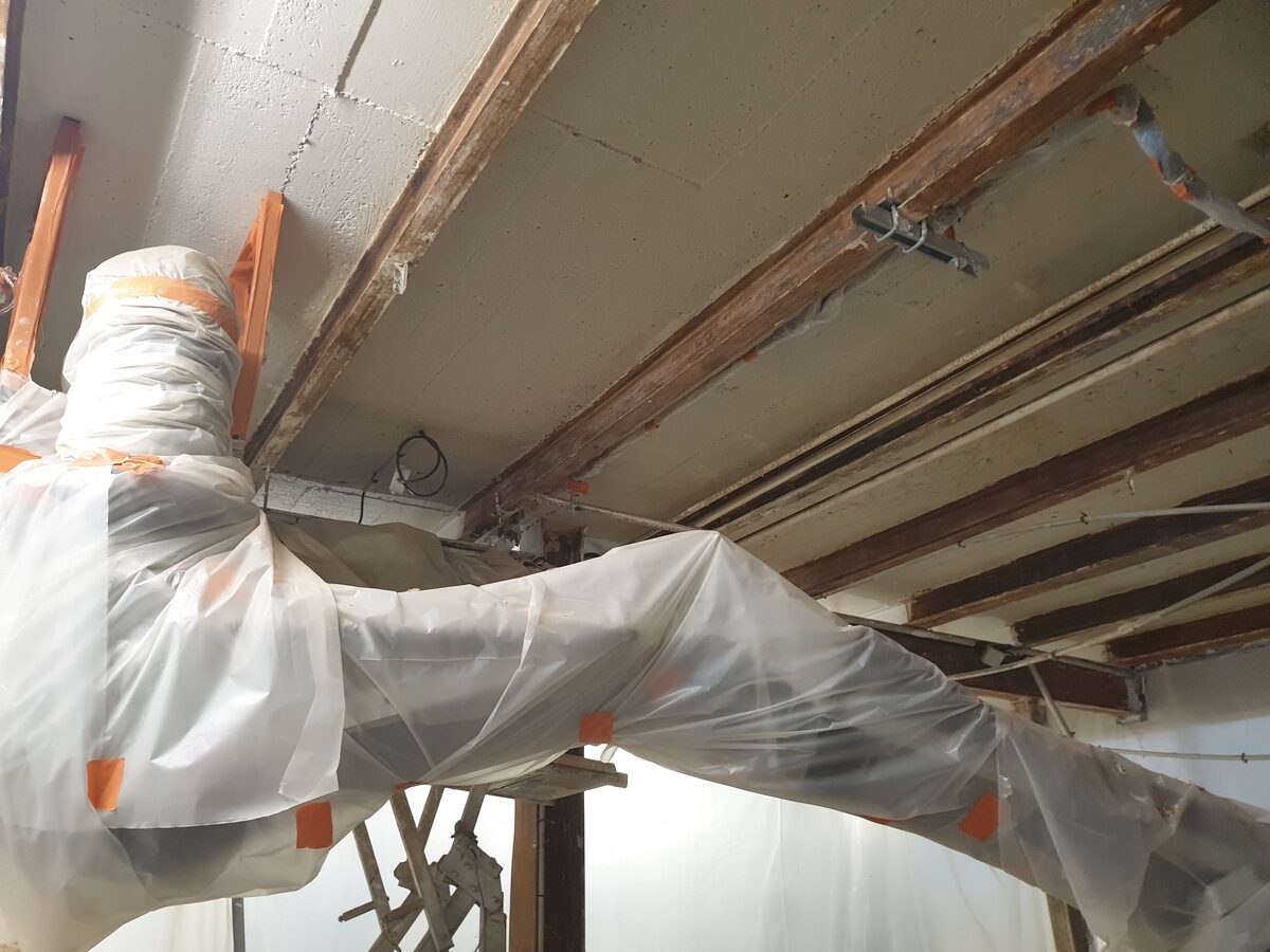 Opérateur en combinaison calfeutrant une zone de travaux sous polyane, gaine d'extraction d'air en place, avant déplombage par décapage chimique.