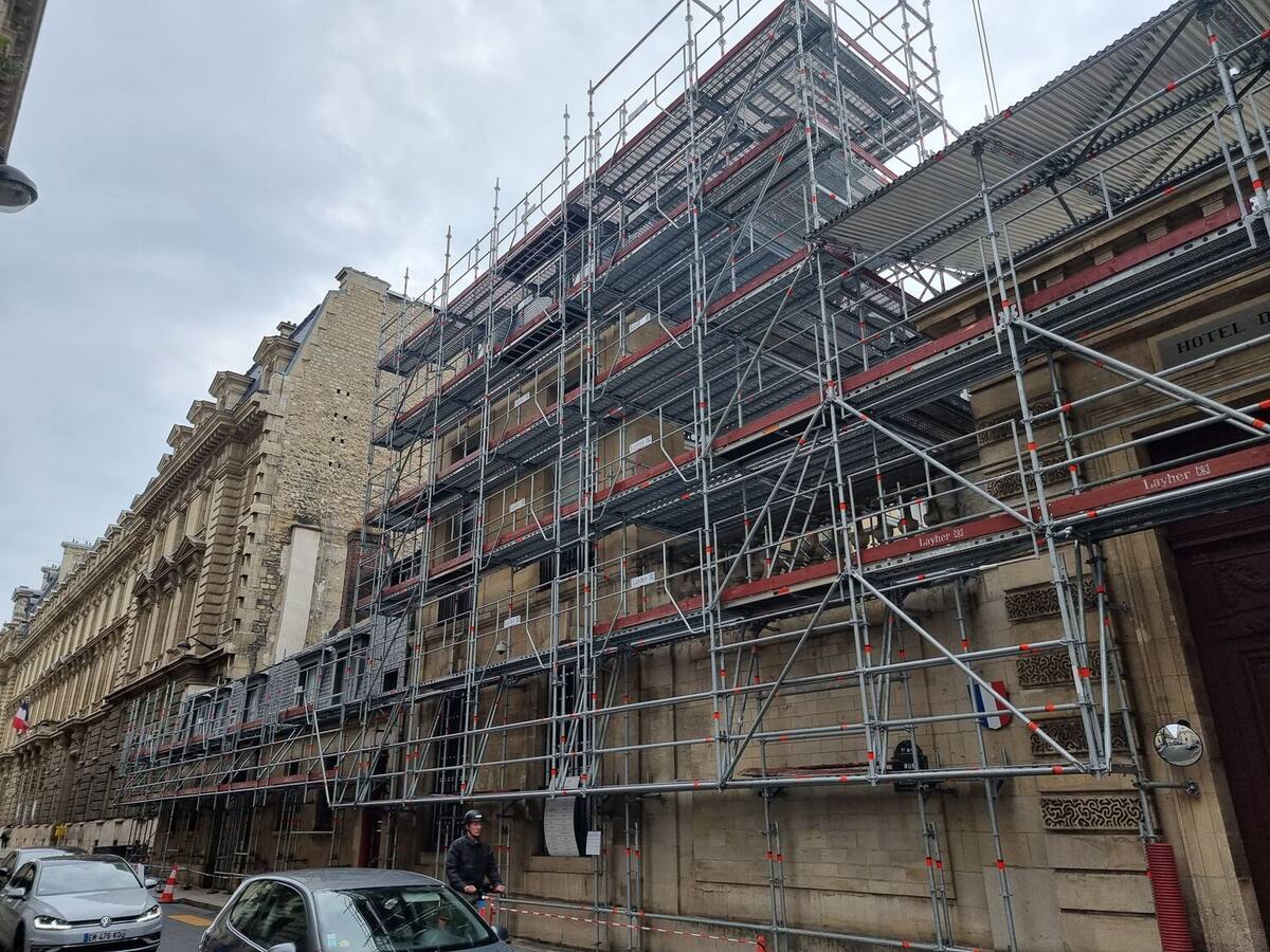 Échafaudage de pied monté sur toute la longueur d'une façade en pierre de taille, en pleine rue.
