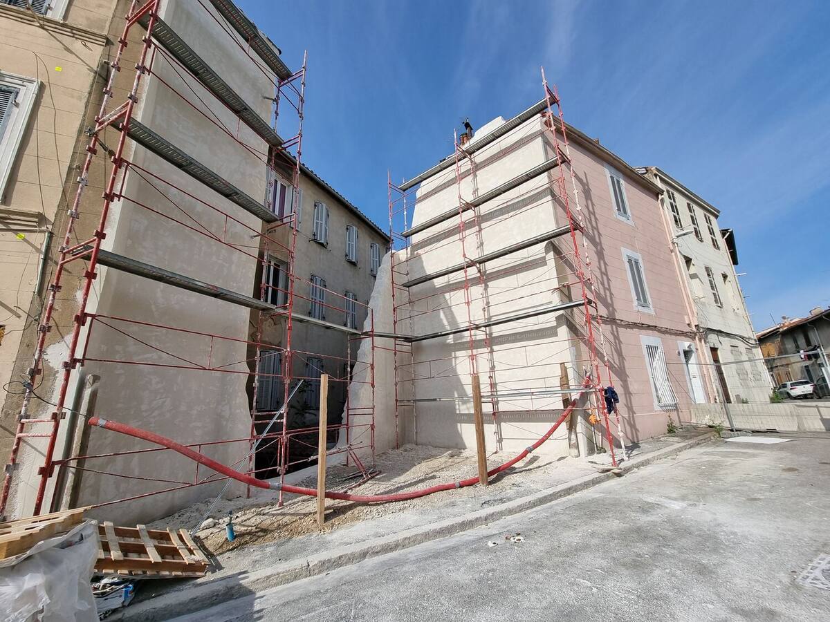 Immeubles mitoyens protégés par des échafaudages rouges dans une rue étroite avant démolition.