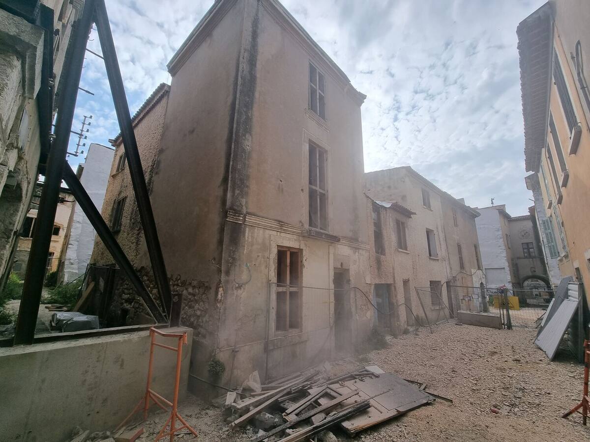 Façade d'un immeuble ancien maintenue par des étais métalliques obliques pendant la démolition des bâtiments voisins, poussière en suspension.