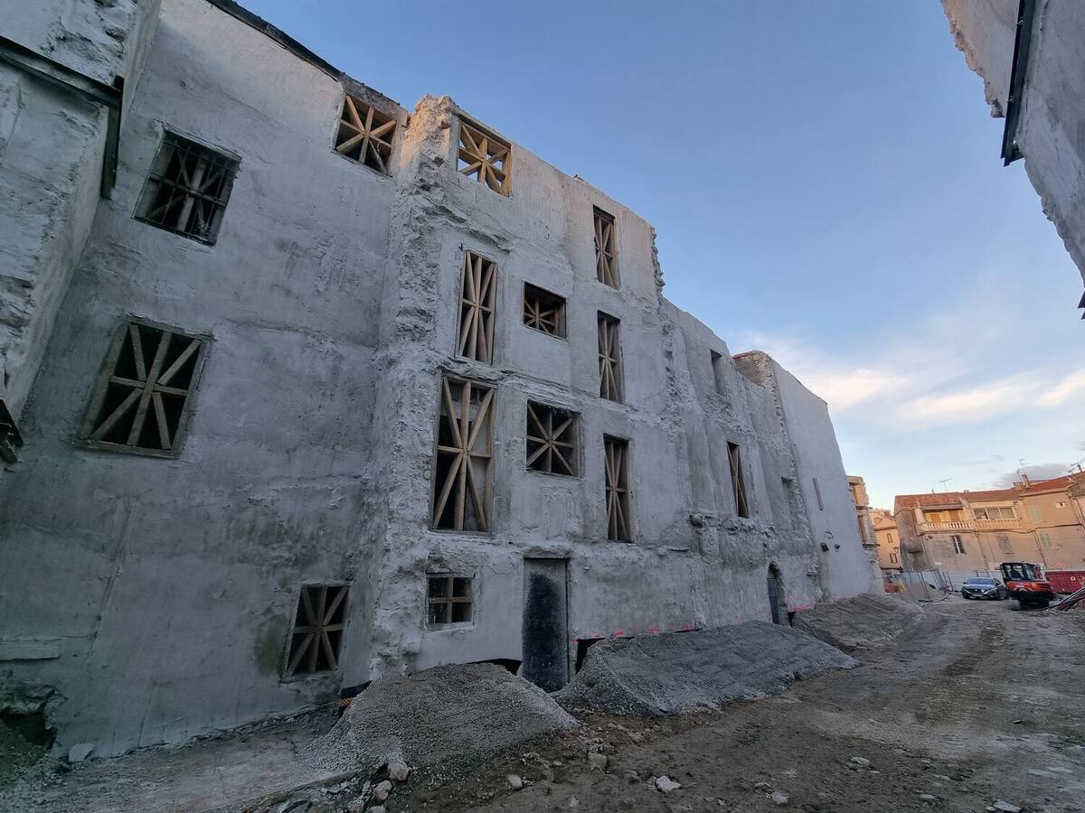 Façades d'immeubles conservées, baies fermées par des croix de Saint-André en bois et parois traitées au béton projeté.