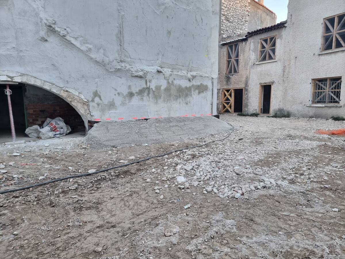 Cour de chantier avec une voûte maçonnée conservée et des murs confortés au béton projeté.