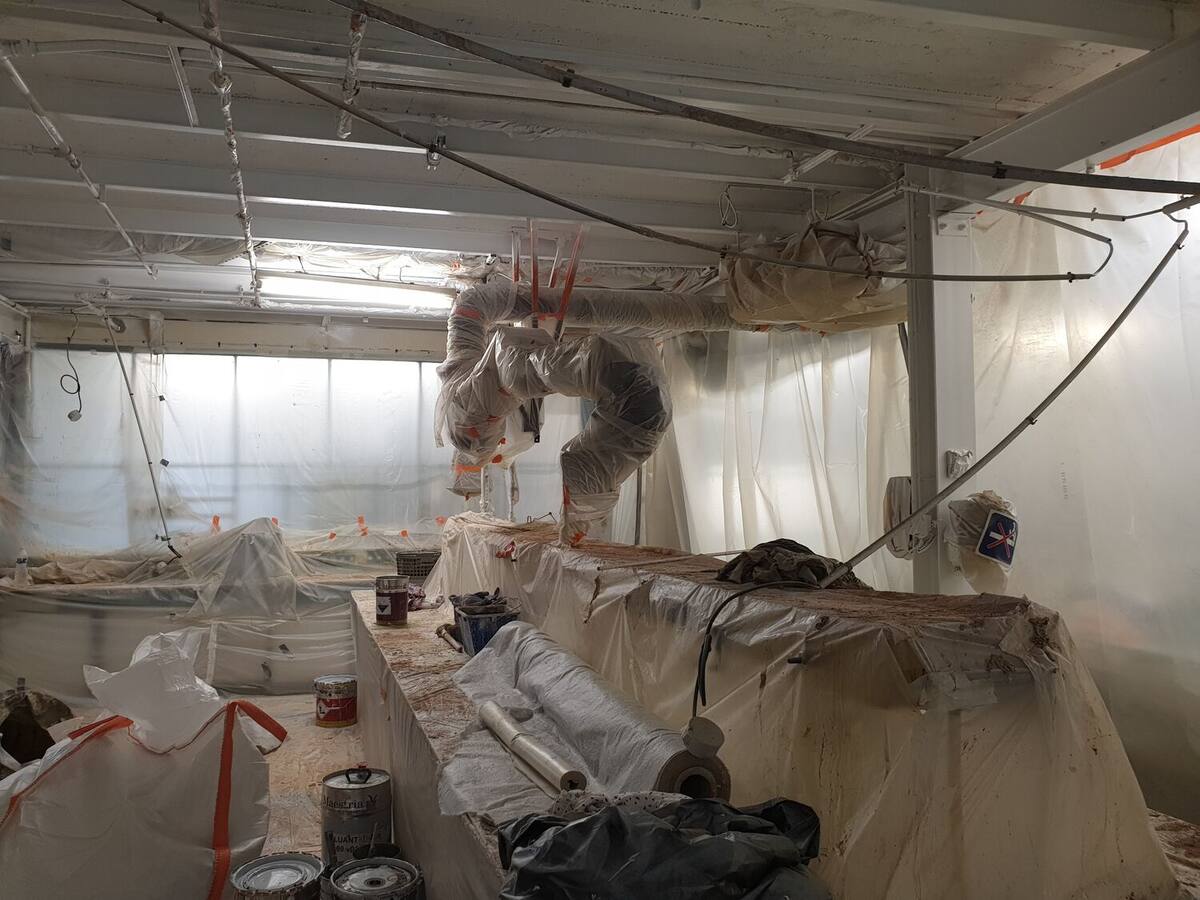 Local de travaux entièrement confiné sous film polyane, avec gaines d'extraction d'air suspendues et mobilier protégé, en attente de déplombage.